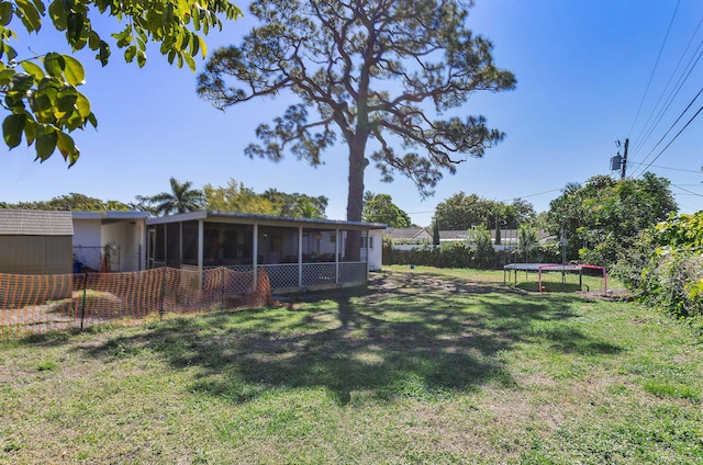 view of yard featuring a sunroom, a trampoline, and fence