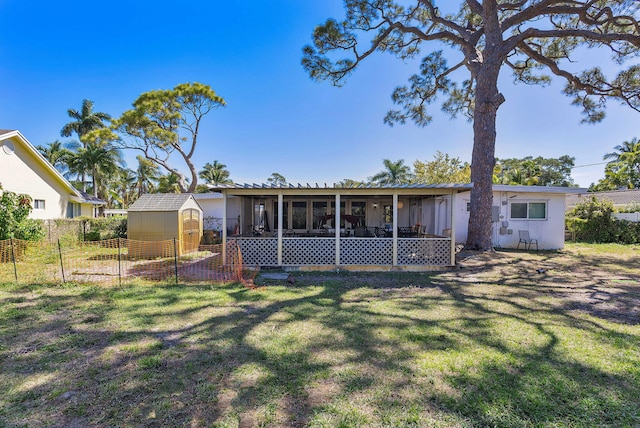 rear view of house featuring an outbuilding, a sunroom, a lawn, and fence