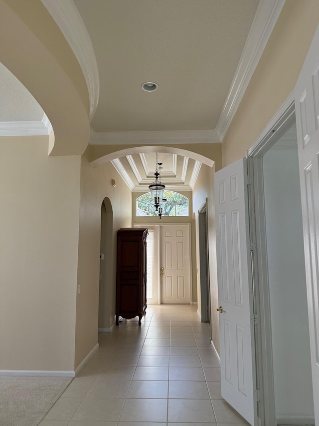 interior space with baseboards, arched walkways, a tray ceiling, crown molding, and light tile patterned flooring