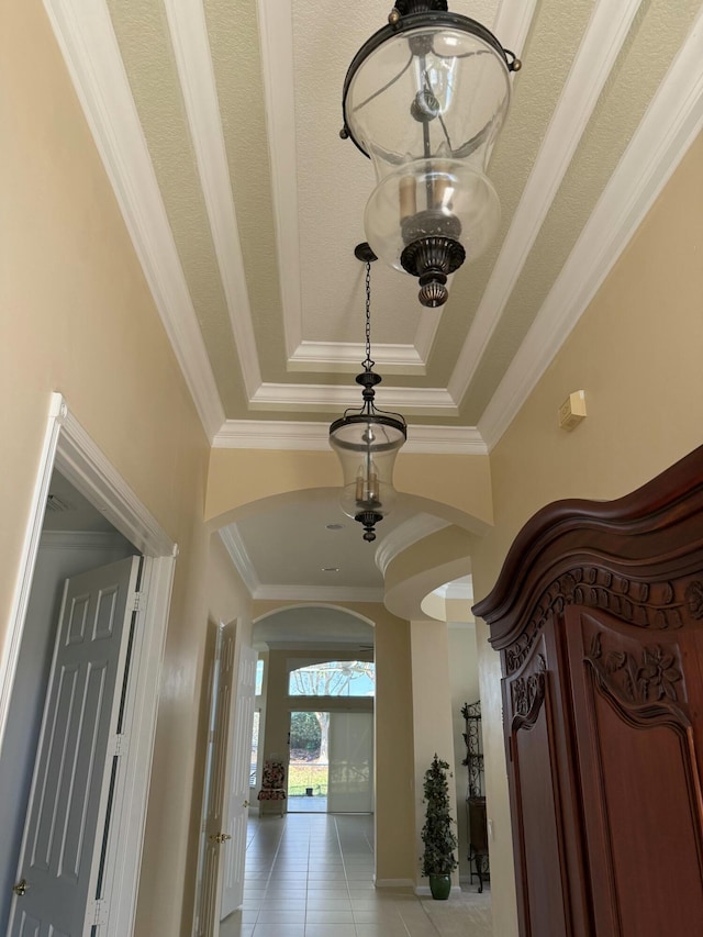 hall featuring ornamental molding, a tray ceiling, light tile patterned floors, and arched walkways