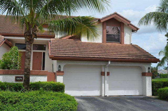 view of front of home featuring aphalt driveway, a tile roof, a garage, and stucco siding