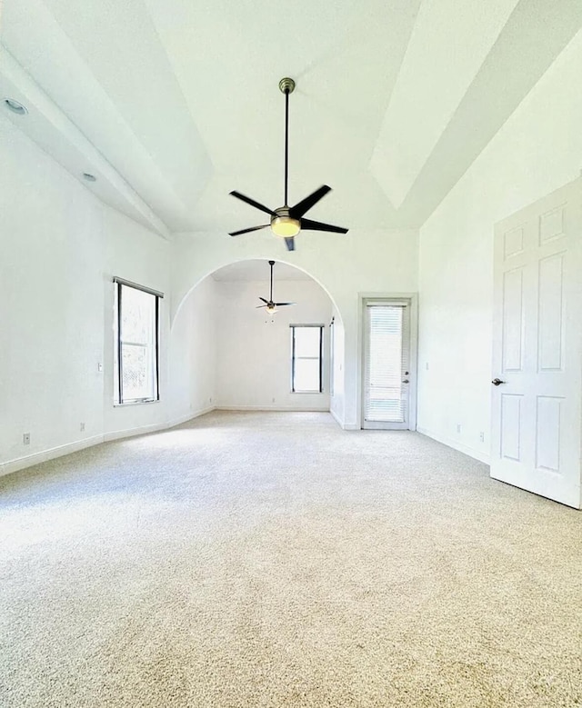 spare room with arched walkways, ceiling fan, high vaulted ceiling, light colored carpet, and baseboards