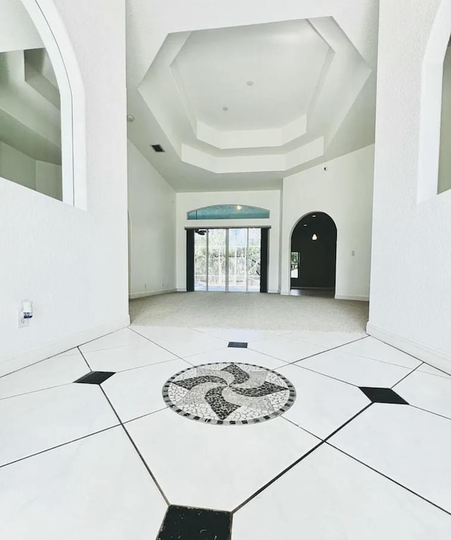 interior space featuring arched walkways, visible vents, a raised ceiling, baseboards, and tile patterned flooring