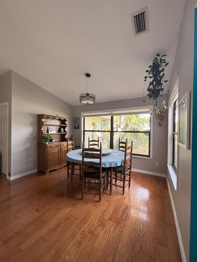 dining area with lofted ceiling, baseboards, visible vents, and wood finished floors