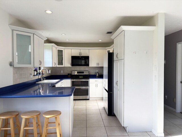 1826 SW Stratford Way, Palm City, FL 34990 - kitchen with black appliances, a peninsula, dark countertops, a sink, and light tile patterned flooring