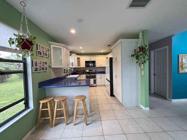 kitchen featuring stainless steel appliances, dark countertops, visible vents, a sink, and a peninsula