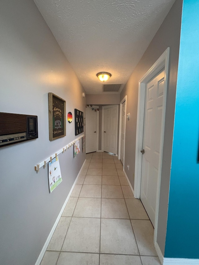 hallway featuring light tile patterned floors, baseboards, visible vents, and a textured ceiling