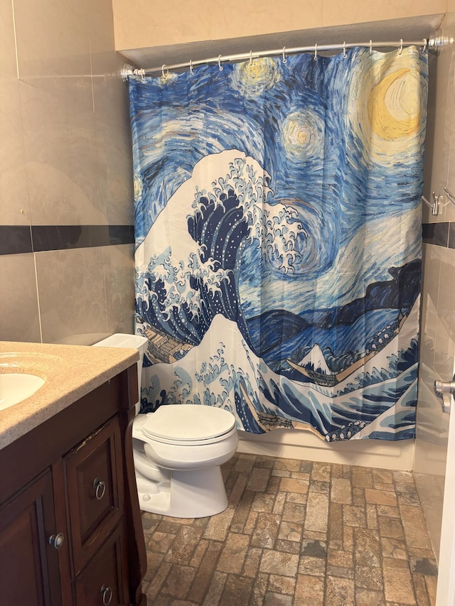 bathroom featuring brick floor, tile walls, toilet, shower / bath combo, and vanity