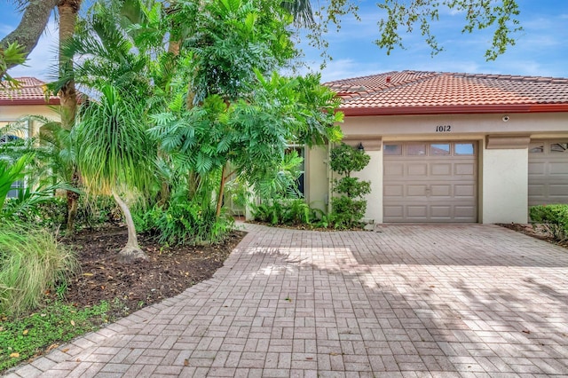 view of front of home with a tiled roof, decorative driveway, an attached garage, and stucco siding