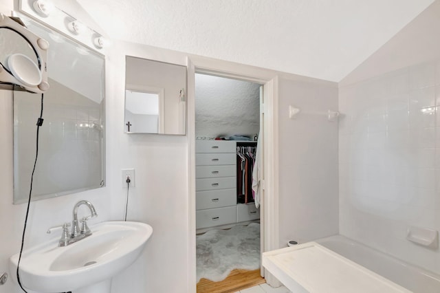 bathroom featuring a textured ceiling, lofted ceiling, walk in shower, and a sink