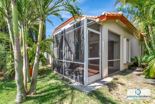 view of side of property featuring a yard, glass enclosure, stucco siding, and a tiled roof