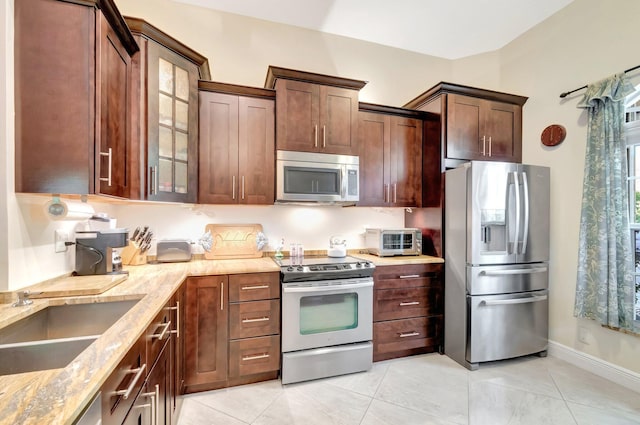 kitchen featuring light stone counters, a toaster, a sink, glass insert cabinets, and appliances with stainless steel finishes