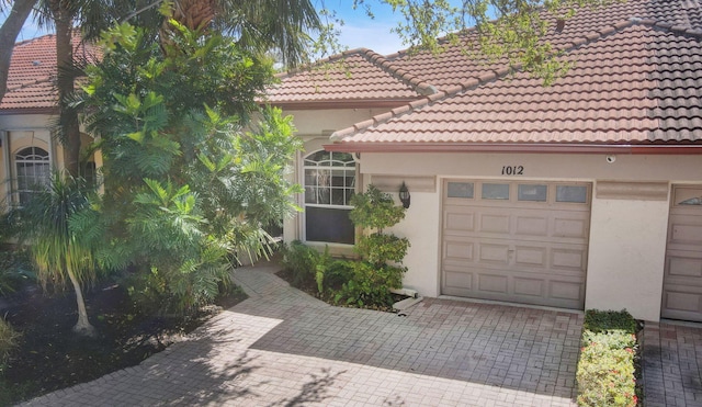 mediterranean / spanish house featuring stucco siding, decorative driveway, an attached garage, and a tile roof