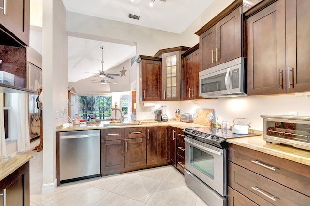 kitchen with visible vents, a sink, light stone counters, stainless steel appliances, and glass insert cabinets