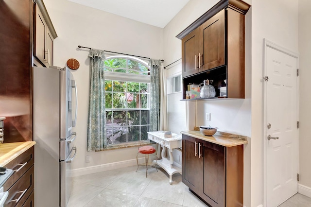 kitchen featuring baseboards, light tile patterned flooring, freestanding refrigerator, light countertops, and dark brown cabinets