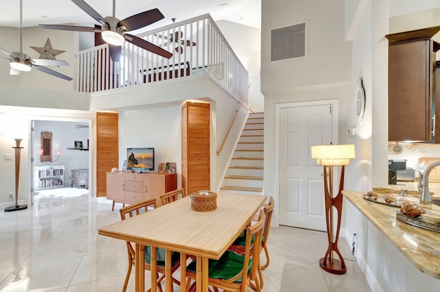 dining area featuring light tile patterned floors, visible vents, ceiling fan, stairs, and a towering ceiling