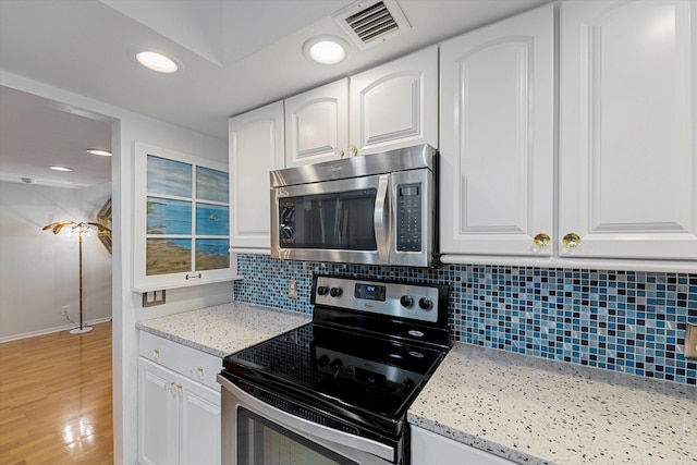 kitchen with visible vents, stainless steel appliances, light wood-type flooring, white cabinetry, and backsplash