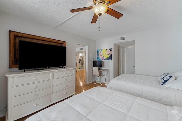 bedroom with ceiling fan, a textured ceiling, visible vents, and wood finished floors