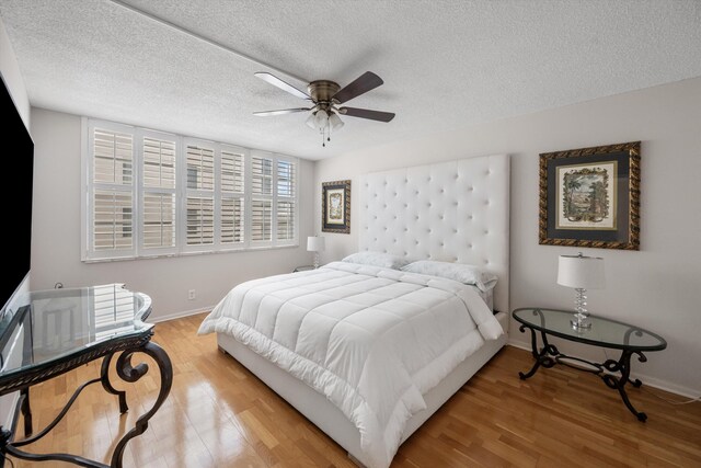 bedroom with light wood-type flooring, a ceiling fan, baseboards, and a textured ceiling