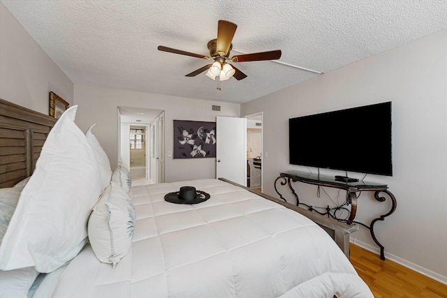 bedroom with a textured ceiling, ceiling fan, connected bathroom, wood finished floors, and visible vents