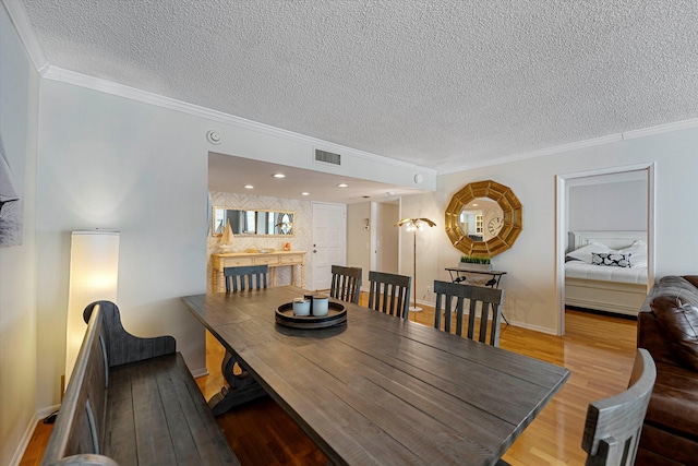 dining space with visible vents, ornamental molding, a textured ceiling, wood finished floors, and baseboards