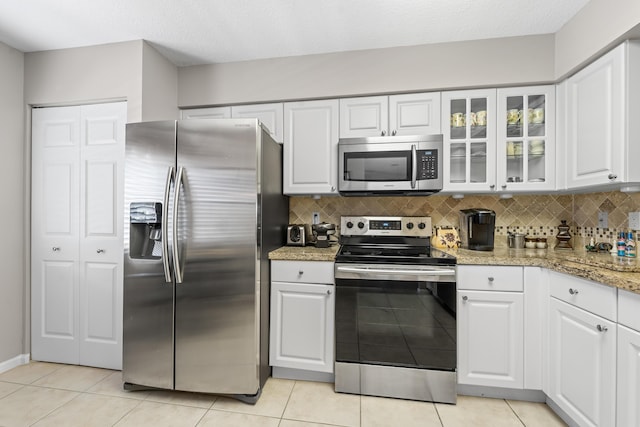 kitchen featuring light tile patterned floors, backsplash, appliances with stainless steel finishes, glass insert cabinets, and white cabinets