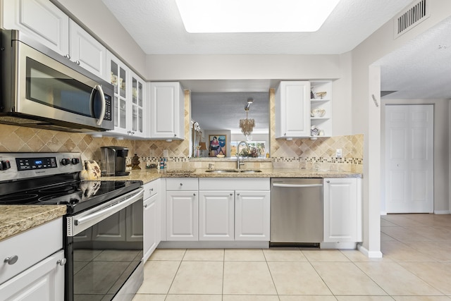 kitchen featuring light tile patterned floors, a sink, visible vents, appliances with stainless steel finishes, and glass insert cabinets