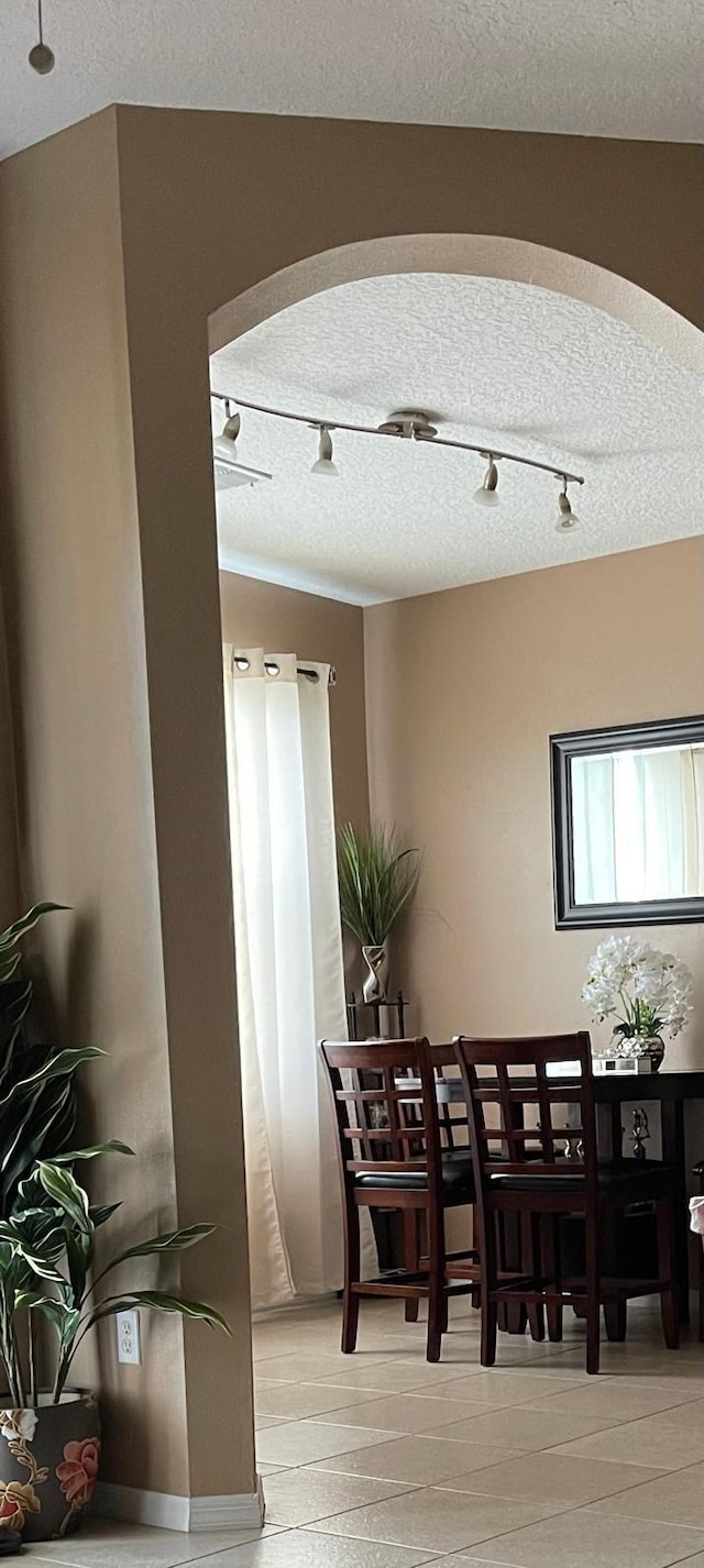 dining area featuring arched walkways, a textured ceiling, and track lighting