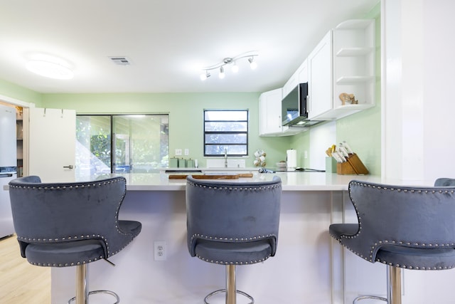 kitchen featuring visible vents, a breakfast bar, open shelves, white cabinetry, and a peninsula