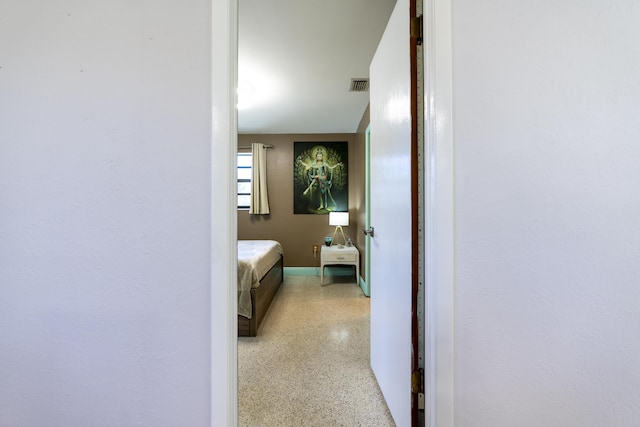 corridor with visible vents, light speckled floor, and baseboards