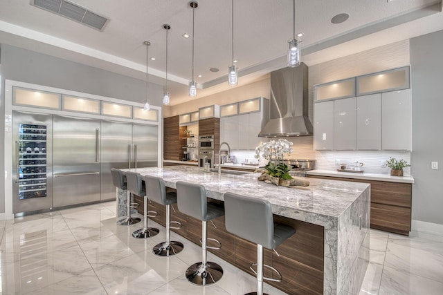 kitchen featuring marble finish floor, tasteful backsplash, a spacious island, visible vents, and wall chimney exhaust hood