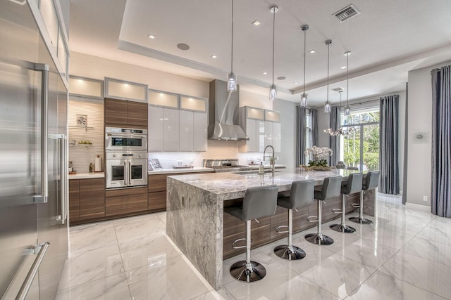 kitchen featuring visible vents, modern cabinets, a tray ceiling, stainless steel appliances, and wall chimney range hood