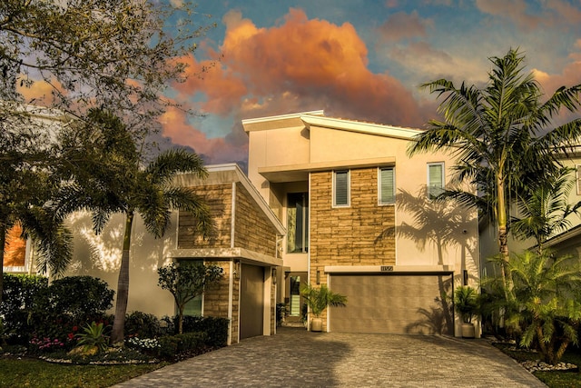 view of front of home featuring stone siding, decorative driveway, an attached garage, and stucco siding