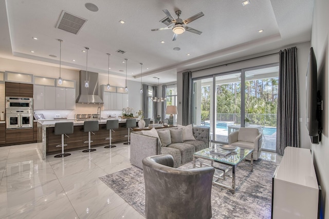 living area featuring marble finish floor, ceiling fan, visible vents, and a raised ceiling