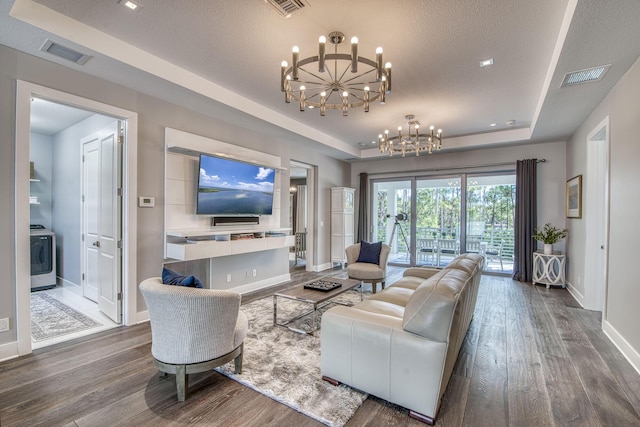 living area featuring a tray ceiling, washer / clothes dryer, visible vents, and an inviting chandelier