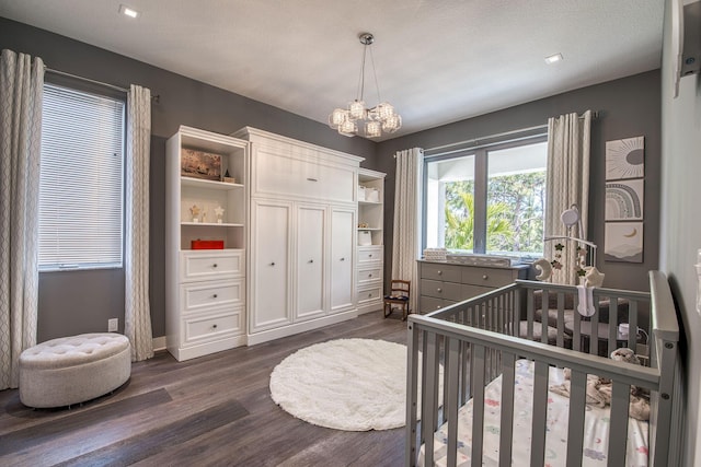 bedroom with dark wood-style floors, a chandelier, and a crib