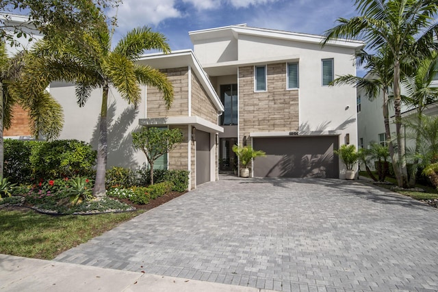 view of front of home featuring stone siding, decorative driveway, an attached garage, and stucco siding