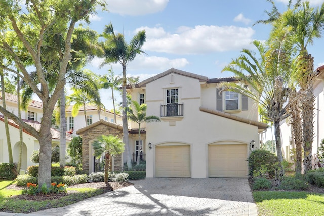 mediterranean / spanish house featuring stucco siding, decorative driveway, an attached garage, a balcony, and a tiled roof