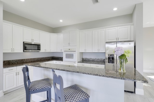 kitchen featuring a breakfast bar, dark stone countertops, white cabinets, and appliances with stainless steel finishes