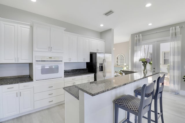 kitchen with dark stone counters, white cabinetry, white oven, a kitchen breakfast bar, and stainless steel fridge