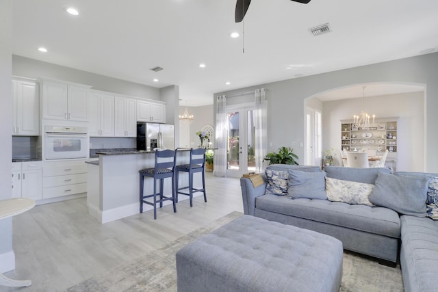 living room with visible vents, recessed lighting, arched walkways, light wood-style floors, and ceiling fan with notable chandelier