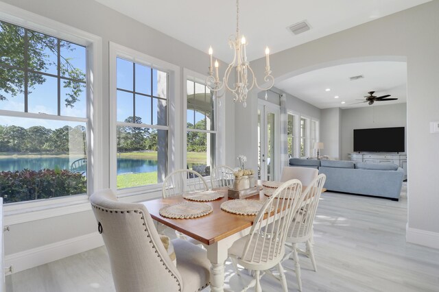 dining room with visible vents, baseboards, light wood-style flooring, ceiling fan with notable chandelier, and arched walkways