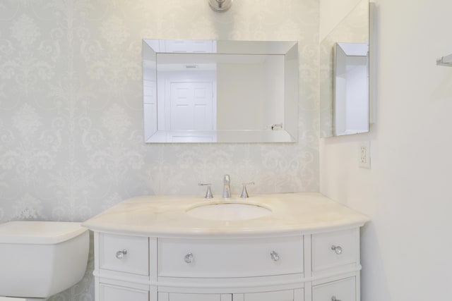 bathroom featuring toilet, vanity, and wallpapered walls