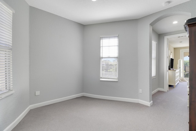 empty room with baseboards, light carpet, arched walkways, and plenty of natural light