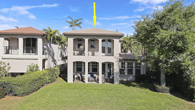 rear view of property featuring stucco siding, a tile roof, a patio, a yard, and a balcony