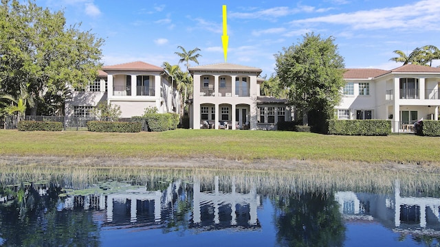 back of property with a water view, a lawn, a balcony, and fence