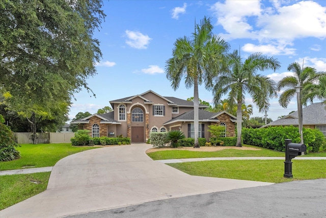 traditional-style home with a front yard, concrete driveway, fence, and stucco siding