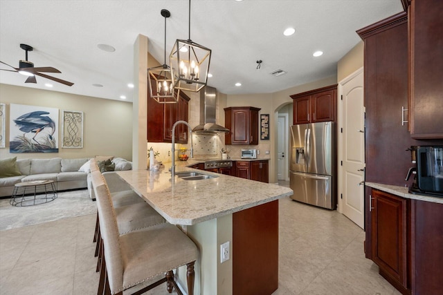 kitchen featuring arched walkways, a peninsula, a sink, stainless steel refrigerator with ice dispenser, and wall chimney exhaust hood