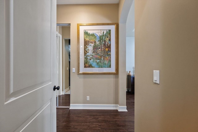 corridor featuring baseboards, arched walkways, and dark wood-style flooring