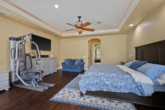 bedroom with visible vents, arched walkways, a raised ceiling, wood finished floors, and crown molding